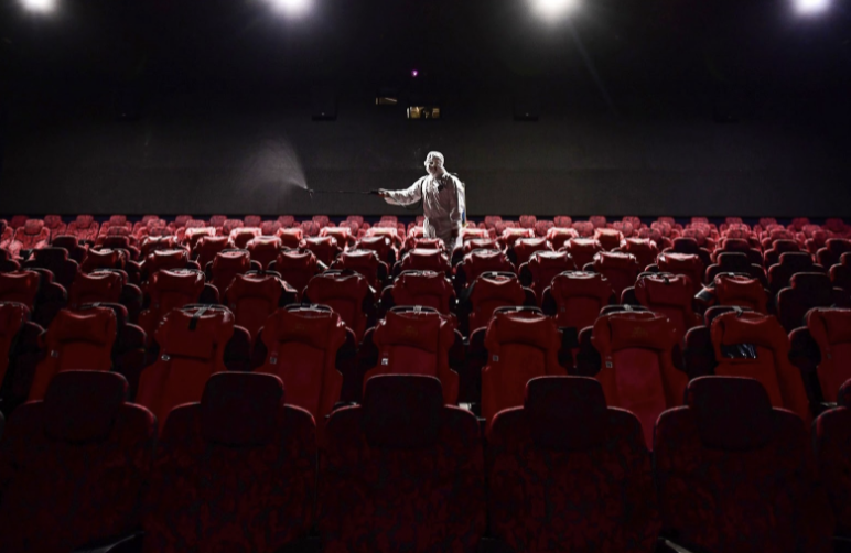 A worker spraying disinfectant in an empty movie theater after public businesses closed.